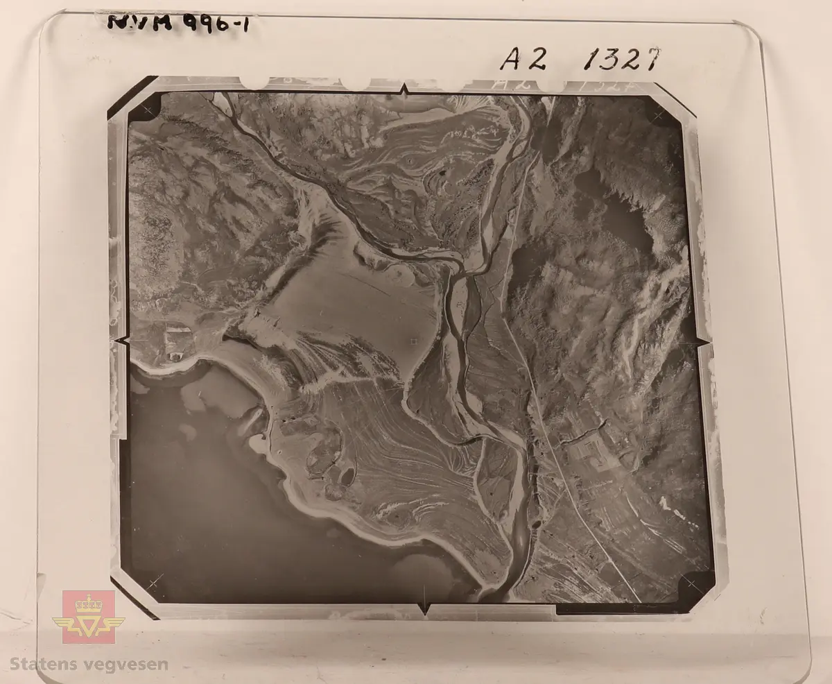 19 stk landskapsfoto på glassplate i svart/hvitt. Fotografiene er flyfoto i fugleperspektiv, langt over selve landskapet. Ligger samlet i en eske i egne små beskyttelses poser av papir. Merket med lapper mellom. 