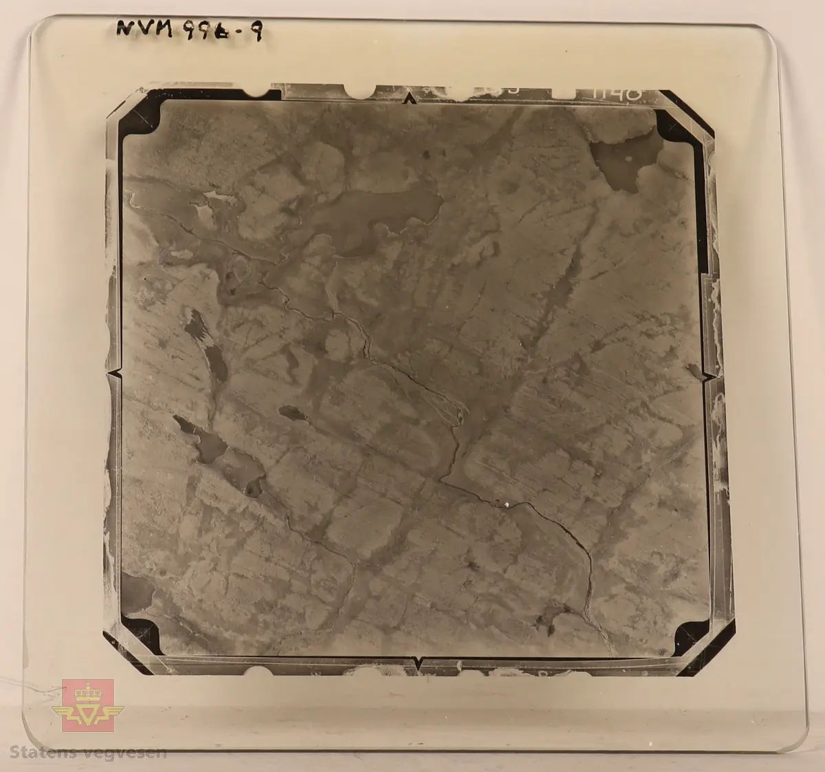 19 stk landskapsfoto på glassplate i svart/hvitt. Fotografiene er flyfoto i fugleperspektiv, langt over selve landskapet. Ligger samlet i en eske i egne små beskyttelses poser av papir. Merket med lapper mellom. 