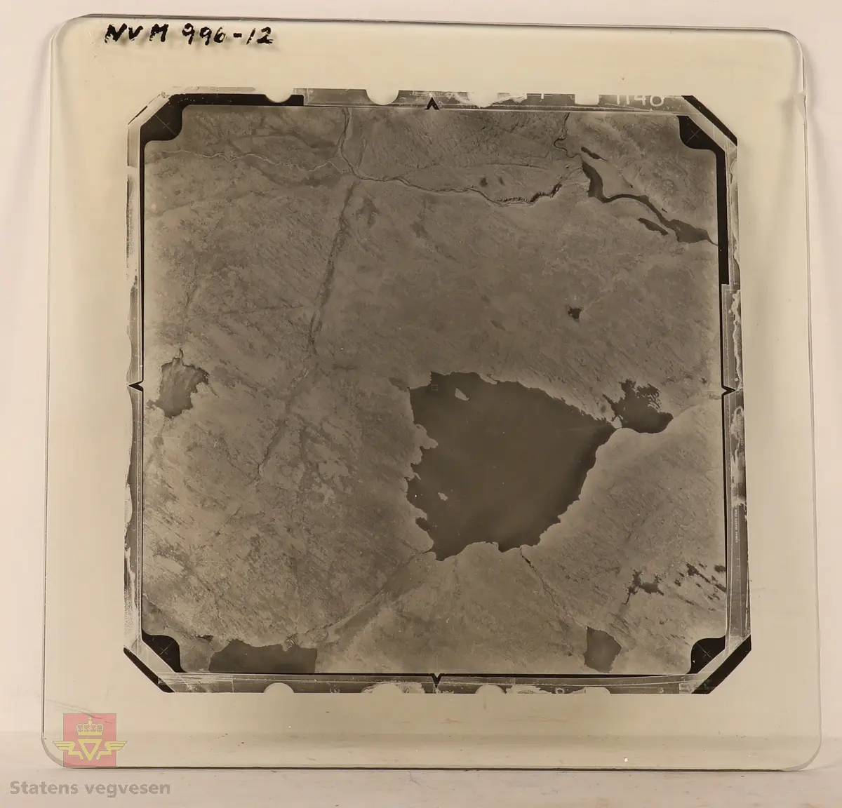 19 stk landskapsfoto på glassplate i svart/hvitt. Fotografiene er flyfoto i fugleperspektiv, langt over selve landskapet. Ligger samlet i en eske i egne små beskyttelses poser av papir. Merket med lapper mellom. 