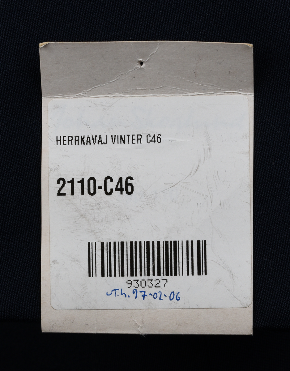 Kavaj i mörkblått tyg av ylle och polyester. Enkelknäppt med tre knappar i gulmetall. Framtill en bröstficka på vänster sida och två midjefickor, varav den på höger sida har lock. Broderat tjänstetecken vid bröstfickan. Vit lapp med svart text vid vänster ärmslut: "HERRKAVAJ VINTER C46
2110-C46
[streckkod] 930327
Ut.h. 97-02-06".
Fyra innerfickor, två på varje sida. Fastsydd vid lapp med svart text på vänster insida, mellan innerfickorna: 
"YTTERTYG
ULL, WOOL  45%
POLYESTER  55%
FODER, LINING
POLYESTER  100%
[symboler för tvättråd] Maskintvätt 40°, Varmt strykjärn, KLorblekmedel får ej användas, Endast kemtvätt med perkloreten, Får ej torktumlas.
C 46 
Johan Skoglund".
I nacken vit hank för upphängning av kavajen med svart text: "Johan Skoglund".