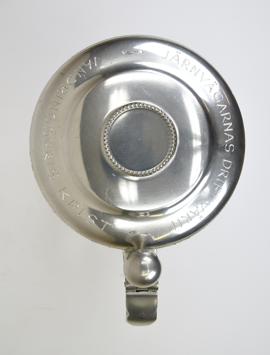 Stop av tenn med ett gängat lock. Stående på fyra kulformade fötter som omsluts av en klo. Svängd hänkel. Blombård runt locket och graverad text på locket "JÄRNVÄGARNAS DRIFTJVÄRN VANDRINGSPRIS KPIST".
Framtill graverad text "NSB" vid ett vinghjul, och text "BEDRIFTSVERNET, HAMAR. Eksjö 16.-17. februar 1952." 
Baktill graverad text:
"1954 2 DVS
1955 HVST ÖR
1956 2 DVS
1957 3. DVS
1958 3. DVS
1959 24. DVS
1960 13 DVS
1961 2 DVS"