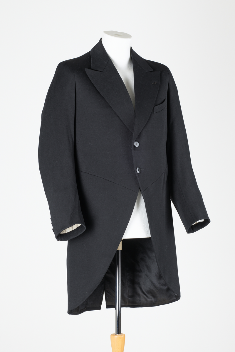 Sjakett av vanlig type. Sort jakke, enkeltspent og med store krageslag. Forstykket har buede kanter og er kortere enn ryggstykket. Ryggstykket har splitt midt bak med to knapper over splitten. Sort fôr i ryggen, hvitt fôr med sort striper inne i ermene.