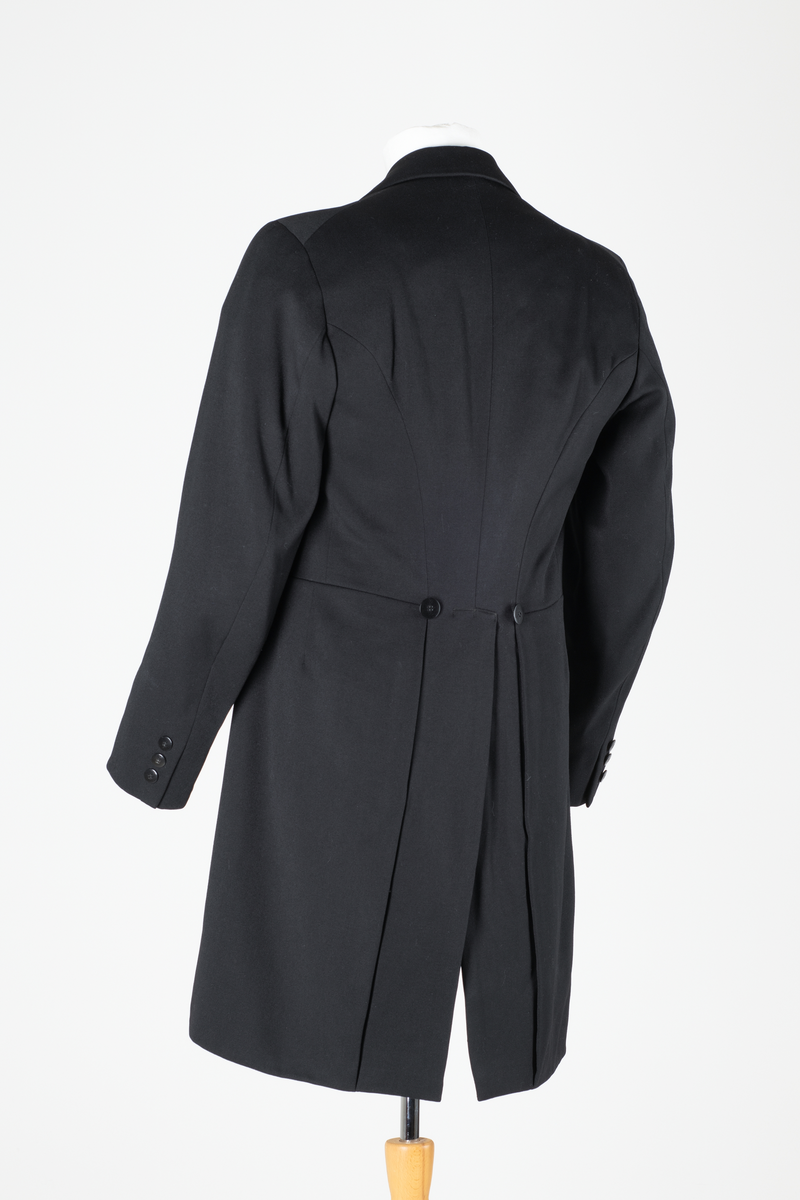 Sjakett av vanlig type. Sort jakke, enkeltspent og med store krageslag. Forstykket har buede kanter og er kortere enn ryggstykket. Ryggstykket har splitt midt bak med to knapper over splitten. Sort fôr i ryggen, hvitt fôr med sort striper inne i ermene.