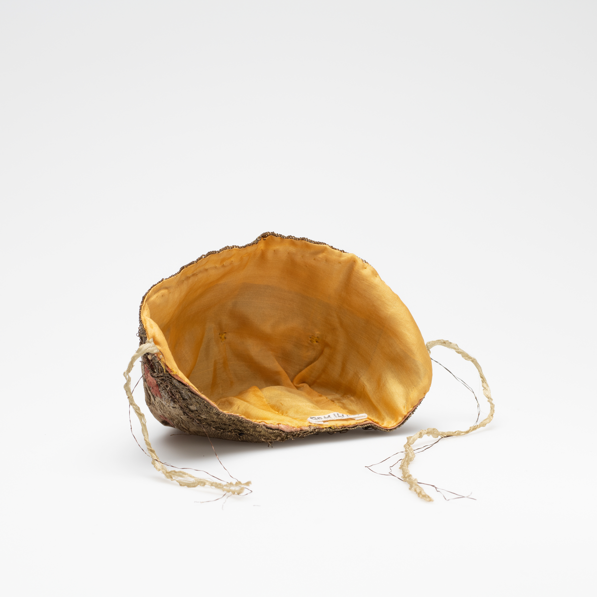 Dåpslue av slike, planterdekor i rødt, grønt og lille på sølvfarget bakgrunn. Dekorert langs kanten med gullfarget blonde i uidentifisert teknik.  Innvendig foret med gul ensfarget silke. Silkebånd på hver side. Lua er sydd sammen av åtte biter.