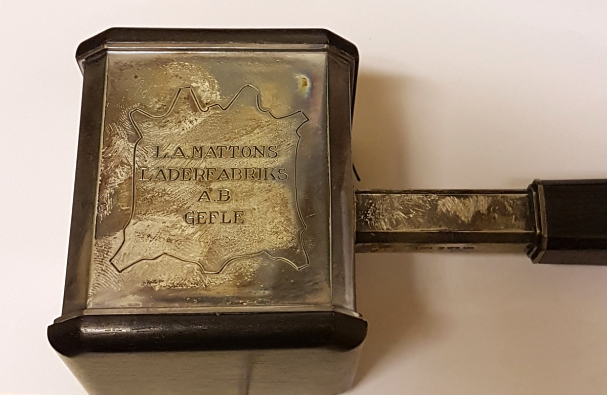 Ordförandeklubba i silver och trä. Ligger i tillhörande etui.  Inskription LA Mattons läderfabrik AB, Gefle. Från tjänstemännen 30/8 1952. Inuti locket står tryckt: Wåhlbergs juvelerarfirma Gävle-Karlstad.
