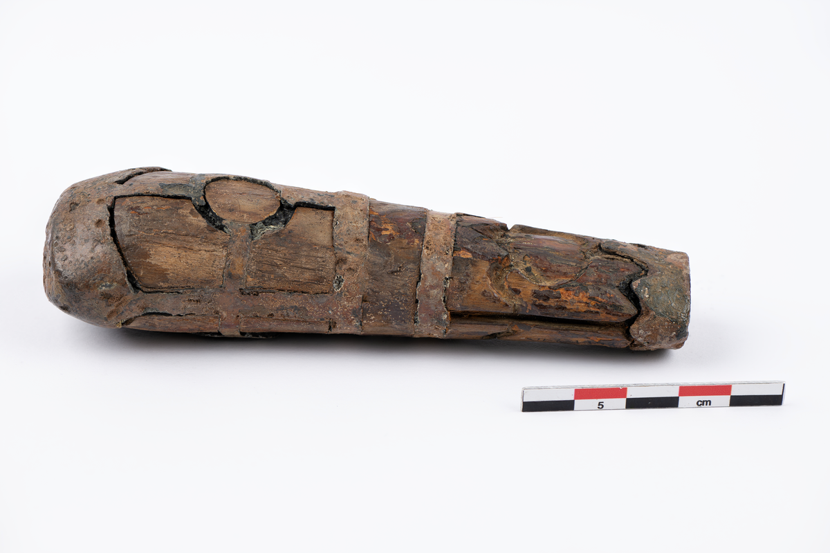 løvtre. tinn. ovalt tverrsnitt. smalner mot falen. beslått med innlagt tinn i mønster. på hver side er i øvre halpart en sirkel hvorfra 4 bånd går ut til rammen. i nedre felt en tulipan med stengel. falen har tenner på oversiden. hullet for tangen firkantet bredde 0,55 lengde 0,7.