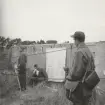 Fyra män vid plansch med organisationsplan utanför kustbunker, Intendenturfältövning Vittsjö, 1961.