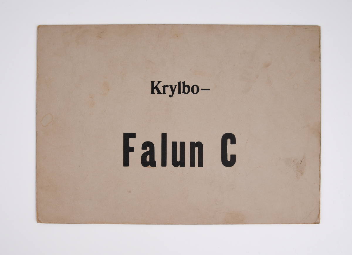 Destinationsskylt av kartong med text i svart "Krylbo - Falun C" på ena sidan och "Falun C - Krylbo" på andra sidan.