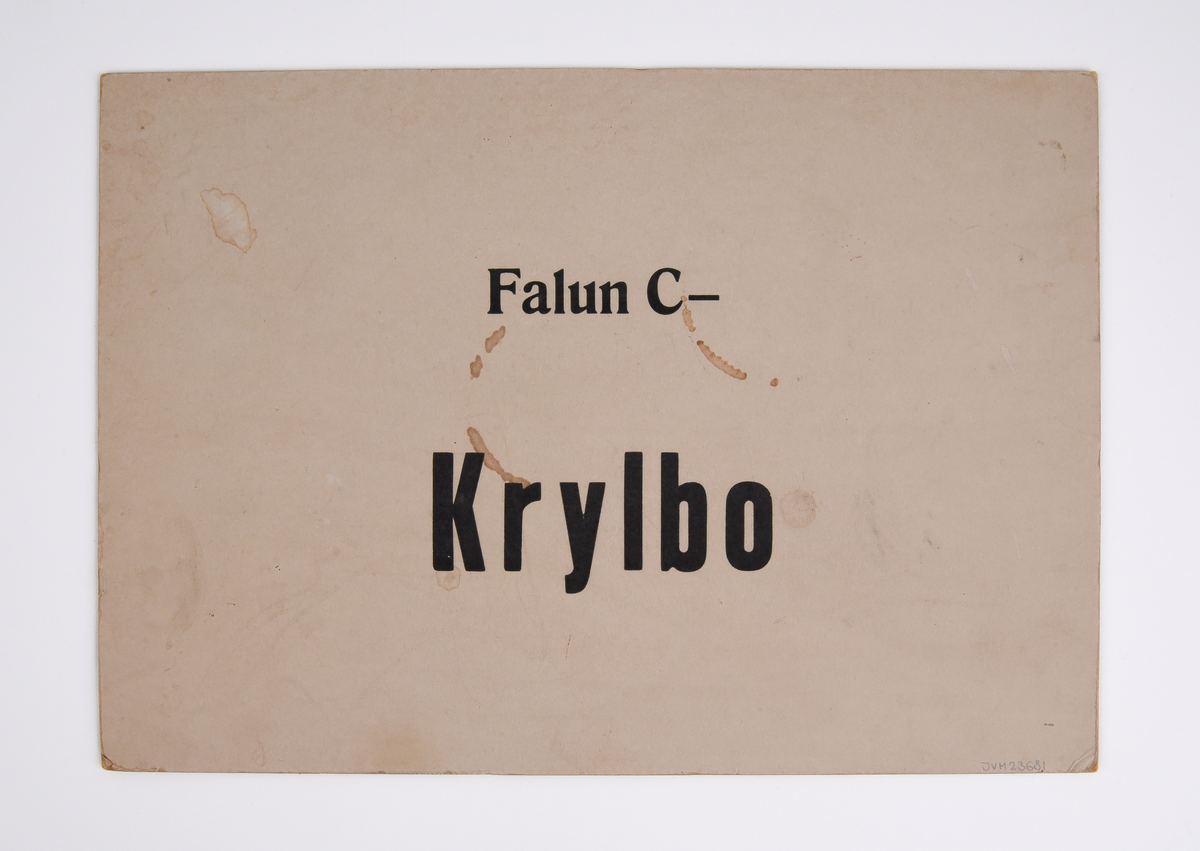 Destinationsskylt av kartong med text i svart "Krylbo - Falun C" på ena sidan och "Falun C - Krylbo" på andra sidan.