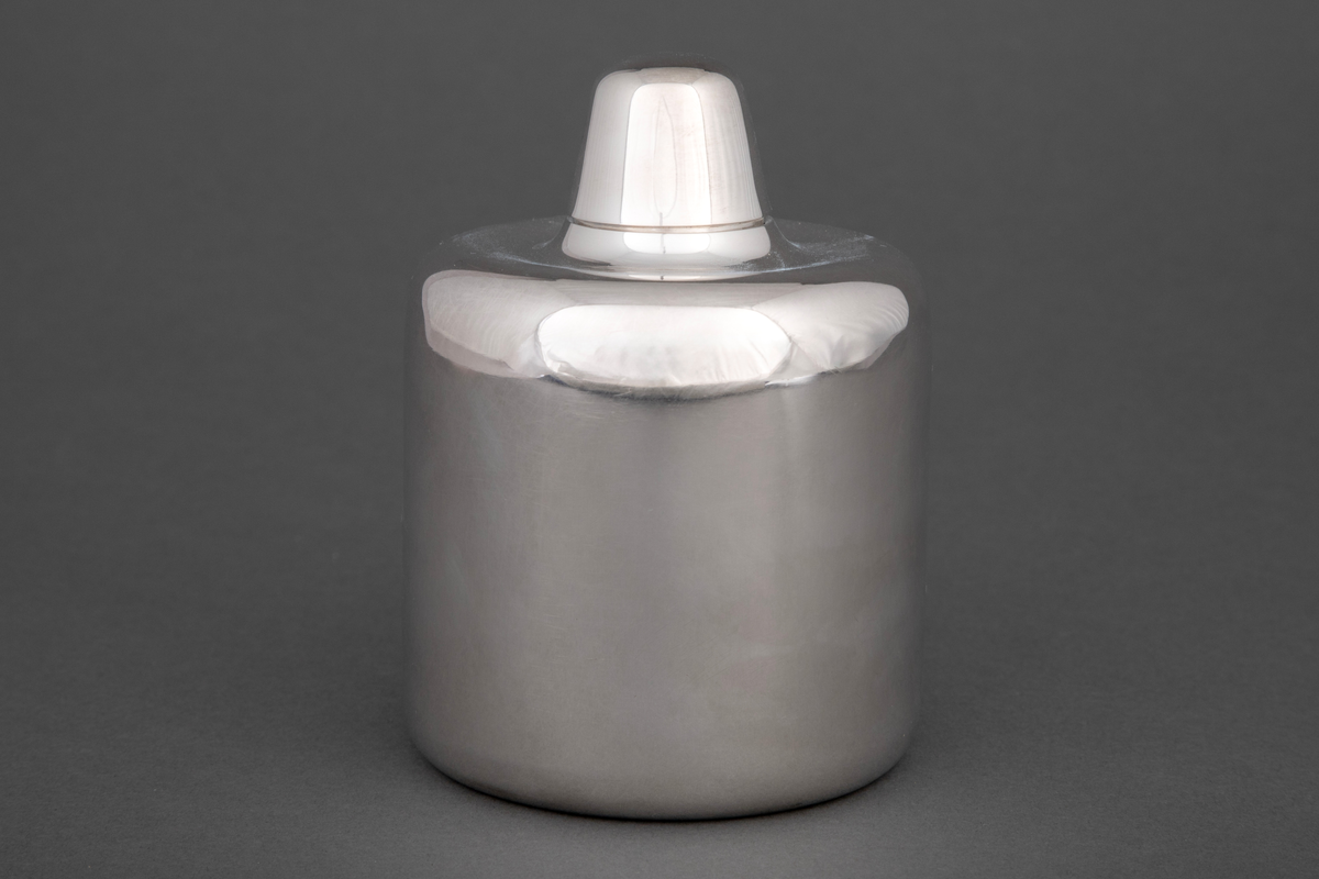 Sylinderformet tedåse i sølv med mykt avrundede kanter. Dåsen avsluttes med et høyt hvelvet lokk, som kan fungere som målebeger for en porsjon te.