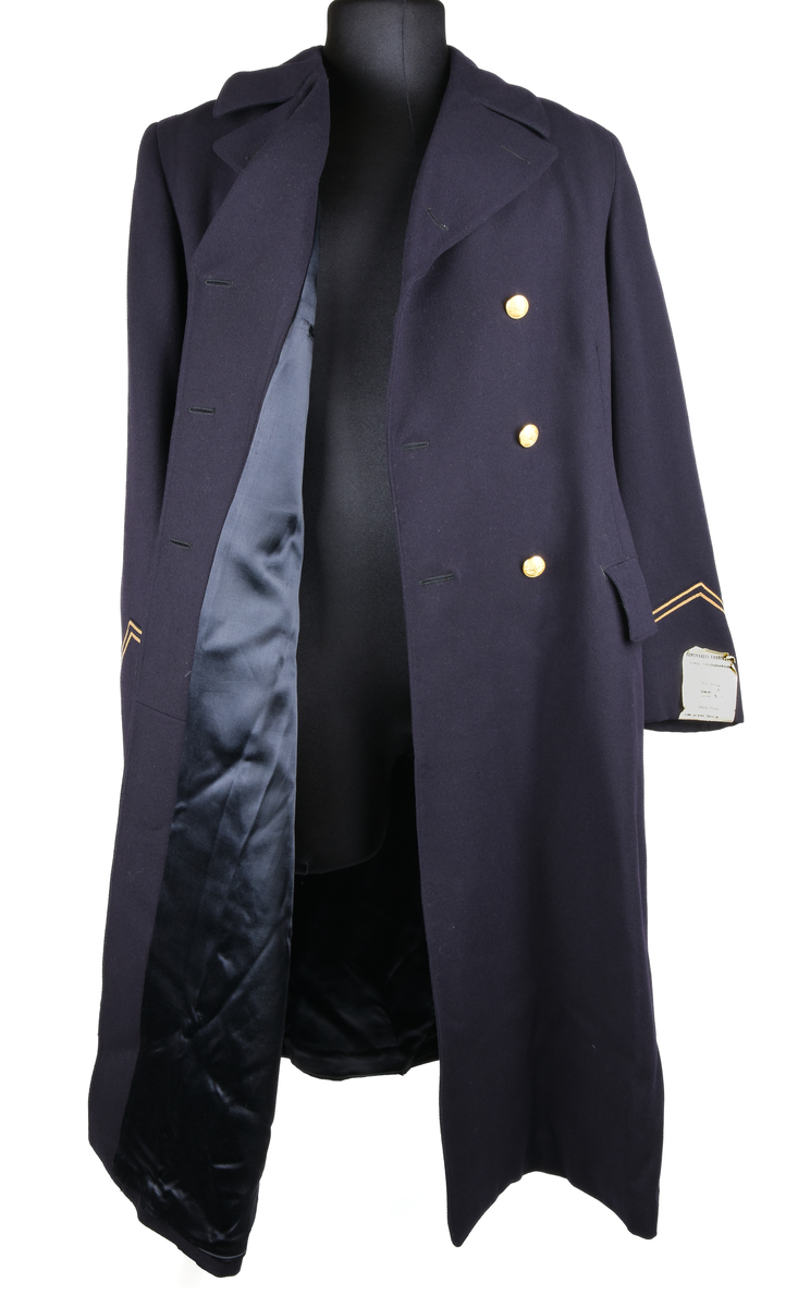 Rock av blått ylle, med sidenfoder. Dubbelknäppt med åtta knappar i gulmetall. Knapparna med krönt vinghjul tillhör 1909 års uniformsreglemente. Framtill två fickor med lock i midjehöjd. Två innerfickor i brösthöjd. Vid kragen en hank för upphängning av kavajen. Baktill sprund och slejf med två knappar. Gradbeteckning för kontorist vid ärmarna. 
Vid vänstra ärm, etikett med text: 
"FÖRSVARETS FABRIKSVERK 
Centrala beklädnadsverkstaden
Order: 23074
Verk: S.J. 24 ts.
Namn: Lindsén 18/4
Adress: Sthlm-Norra
egna galoner lämnade
Grad: Knt.
Tyg nr:
Utförande: Sidenfoder
Mått: 117-64½
Lev. tid:
Anm.:"