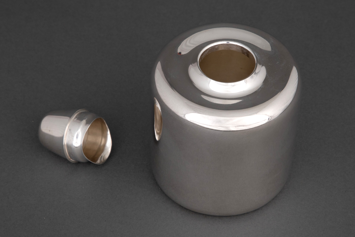 Sylinderformet tedåse i sølv med mykt avrundede kanter. Dåsen avsluttes med et høyt hvelvet lokk, som kan fungere som målebeger for en porsjon te.