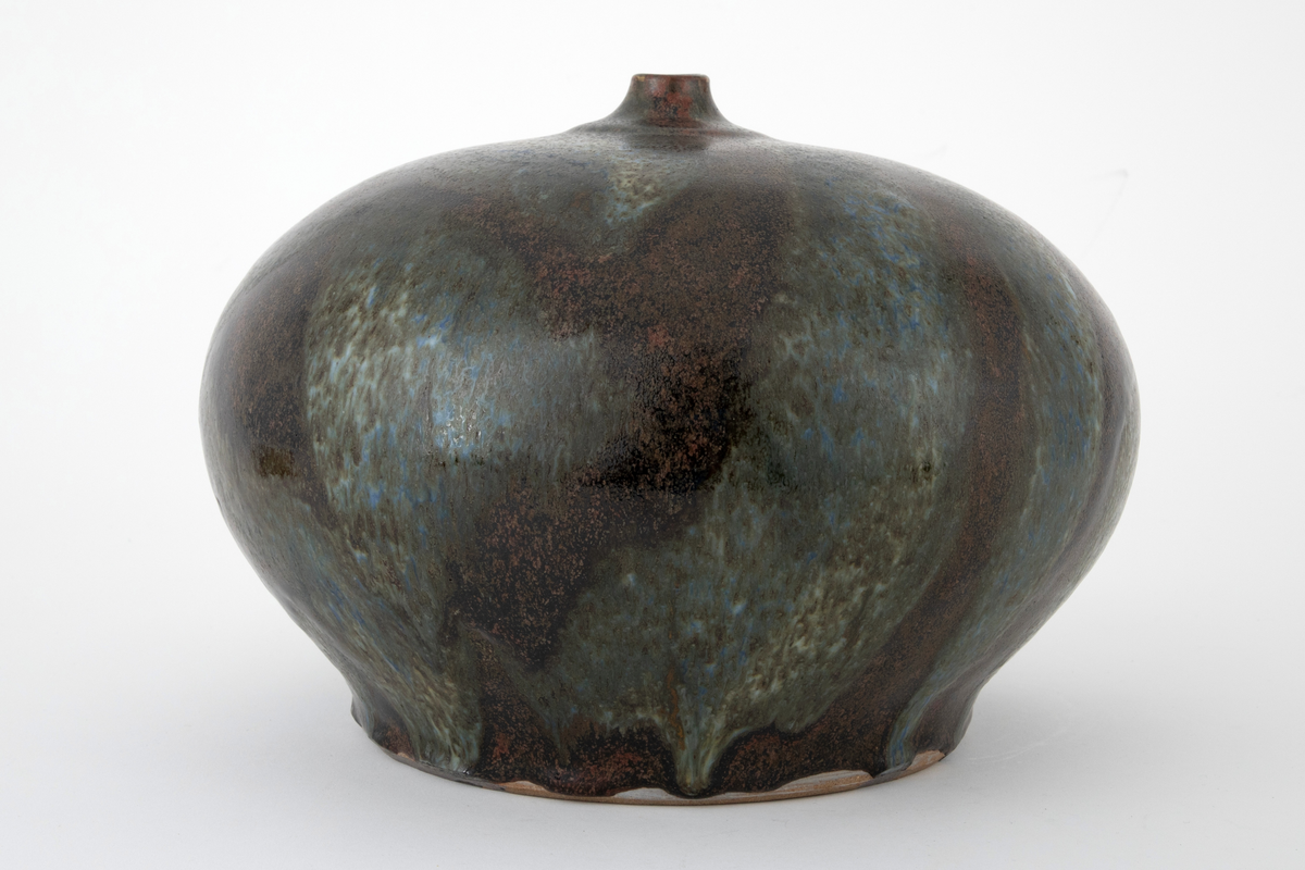 Vase i steingods. Vasen har en glatt, flattrykt kuleform med flat bunn og kort, smal hals. Overflaten er dekket av brun glasur med rennende glasur i blå, grønne og beige nyanser over.
