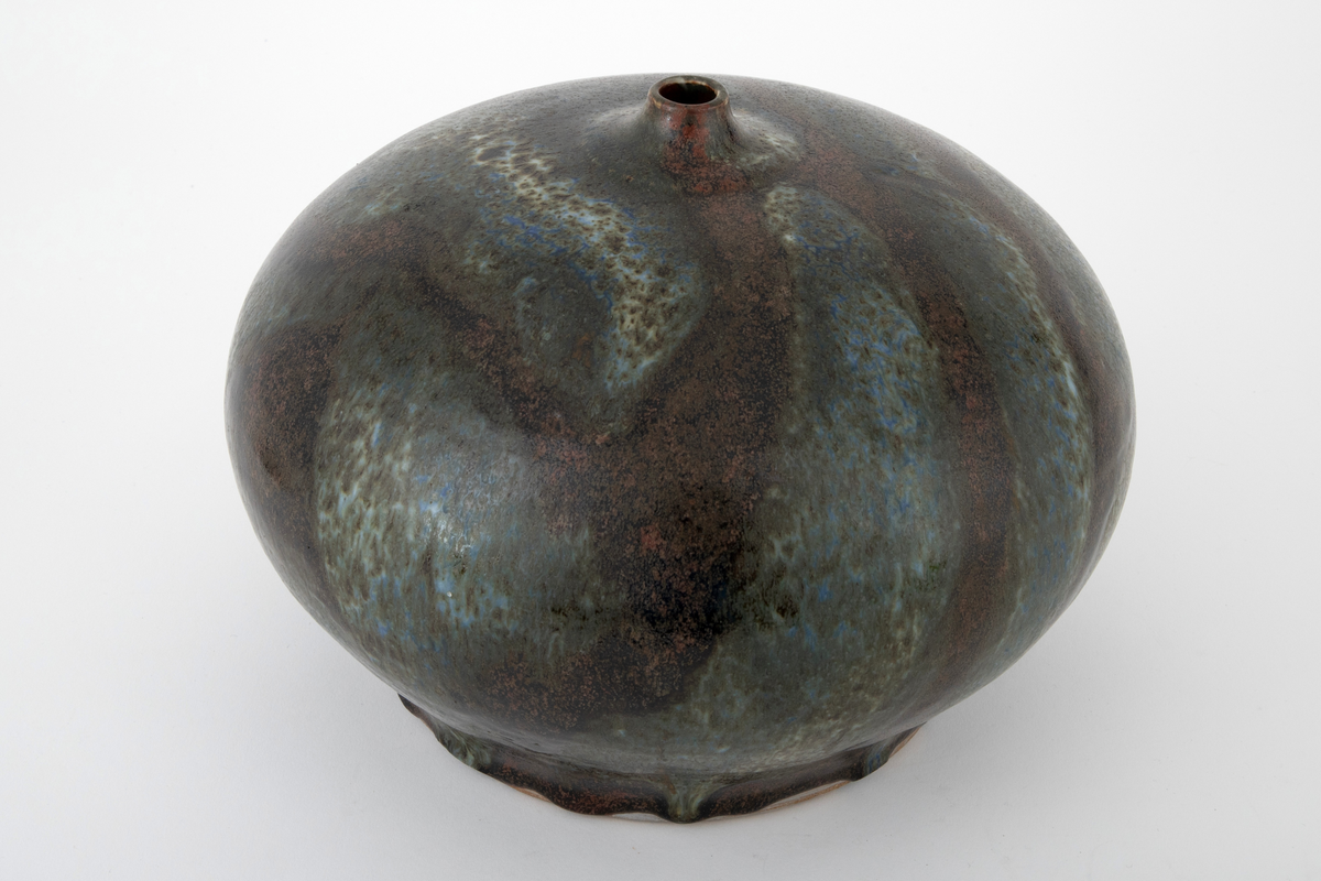 Vase i steingods. Vasen har en glatt, flattrykt kuleform med flat bunn og kort, smal hals. Overflaten er dekket av brun glasur med rennende glasur i blå, grønne og beige nyanser over.
