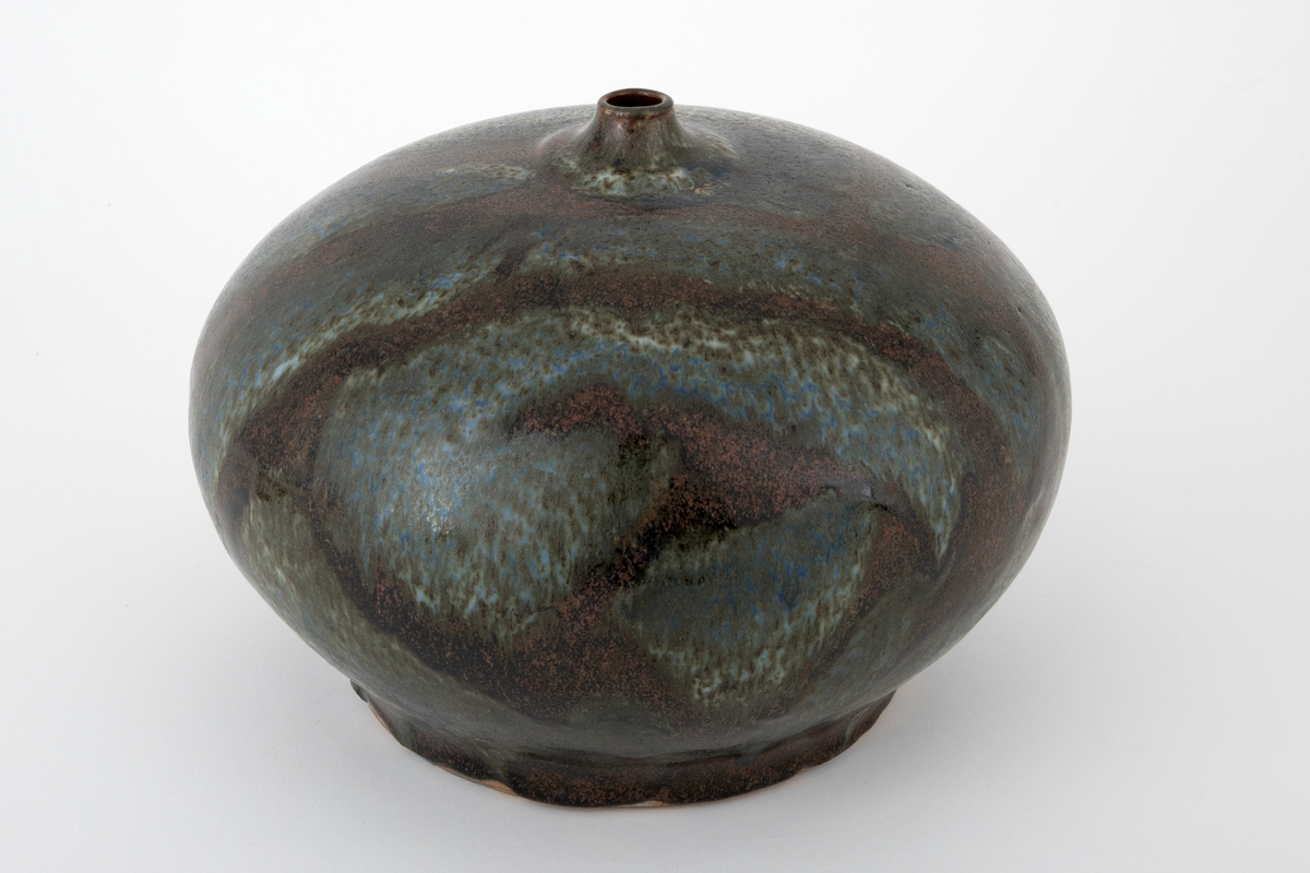 Vase i steingods. Vasen har en glatt, flattrykt kuleform med flat bunn og kort, smal hals. Overflaten er dekket av brun glasur med rennende glasur i blå, grønne og beige nyanser over.