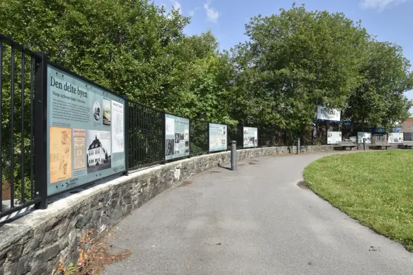 Bildet viser rekkverket langs plassen på toppen av Byparken i Kongsvinger. På rekkverket henger historiske skilt. I bakgrunnen grønne trær, blå himmel.