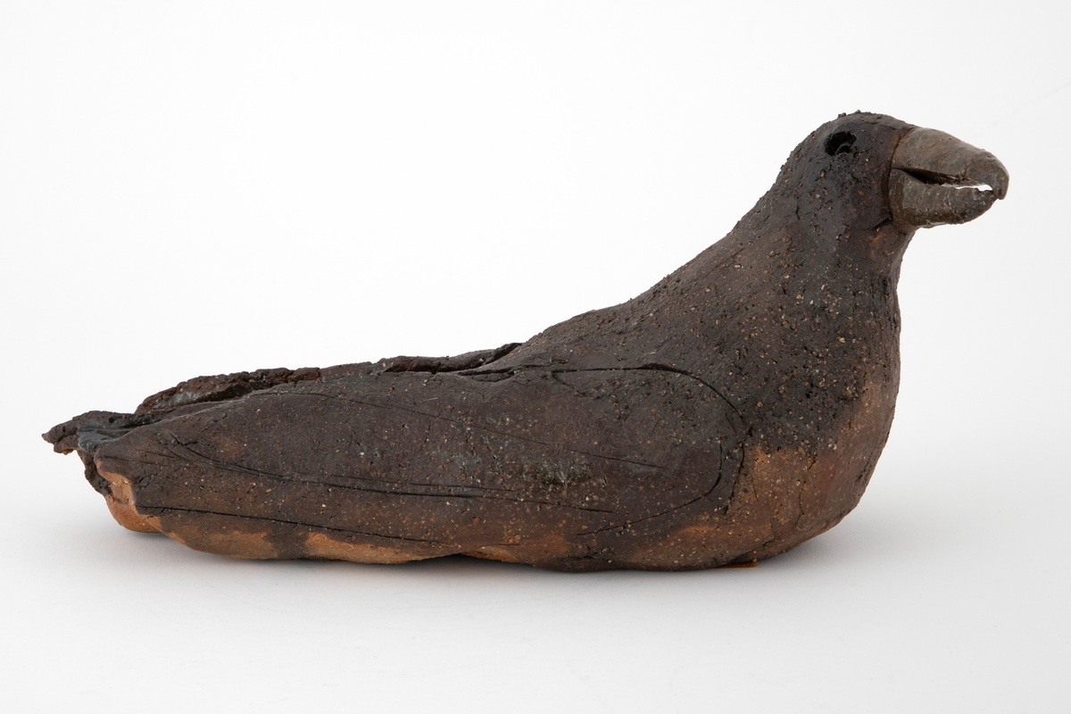Keramikkskulptur forestillende en hvilende måke. Skulpturen er laget av utkjevlet leire som er bøyd sammen og formet. Ujevn overflate med antydning til sprekkdannelser. Grovt gods dekket med mørkebrun, matt glasur. Blank, grønnlig glasur på nebb og enkelte steder på kroppen. Måkens vinger er antydet ved rissing i godset.