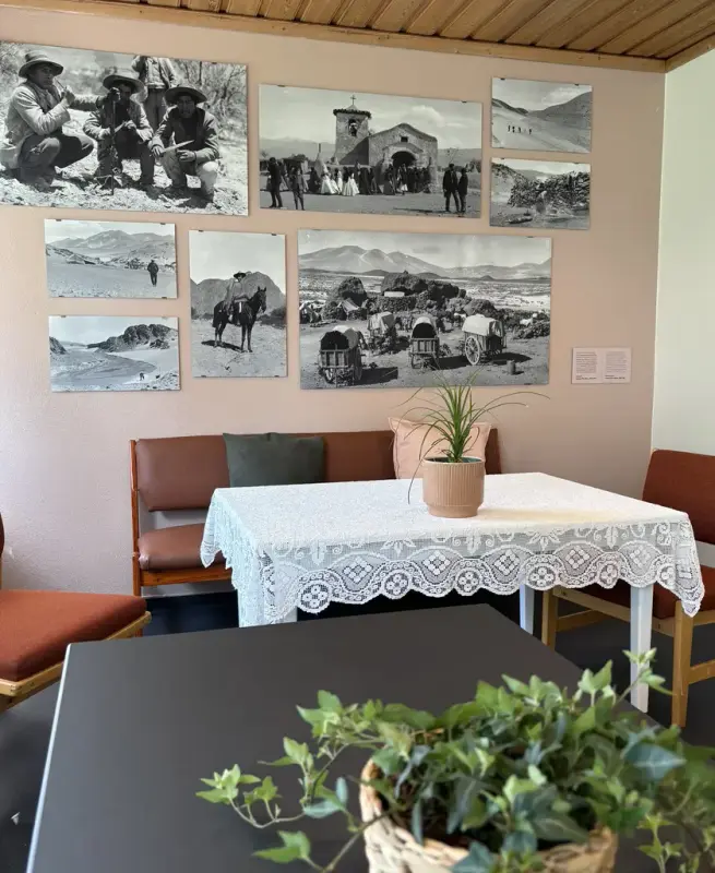 Sofa, bord og stoler. På veggen bak flere sort-hvit bilder med historiske motiver.