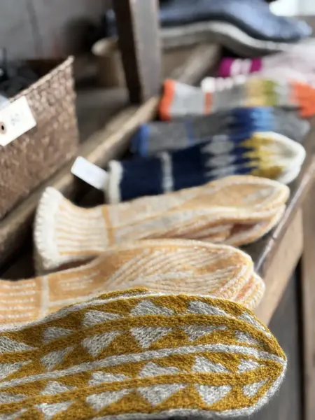 En rekke håndstrikkede votter i flere farger ligger på en hylle