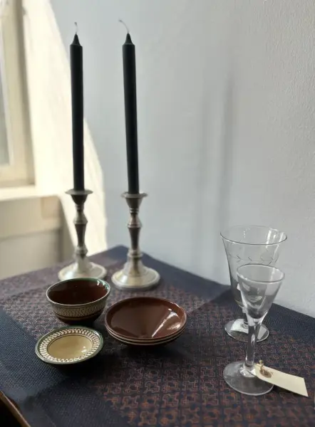 To lysestaker, tre små keramiske boller og to stetteglass står på et bord med en blå, mønstret løper.