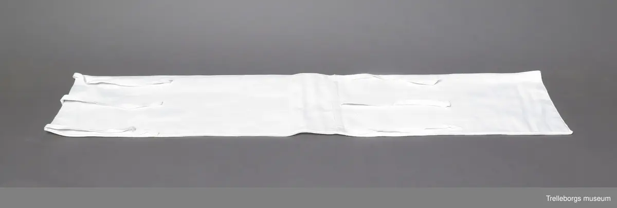 Linda av rektangulärt tygstycke med 3 st 0,8 cm breda band i en kortända (ett i varje hörn och ett i mitten) samt 3 st likandana 40,5 cm från kortändan (ett på varje sida och ett i mitten).