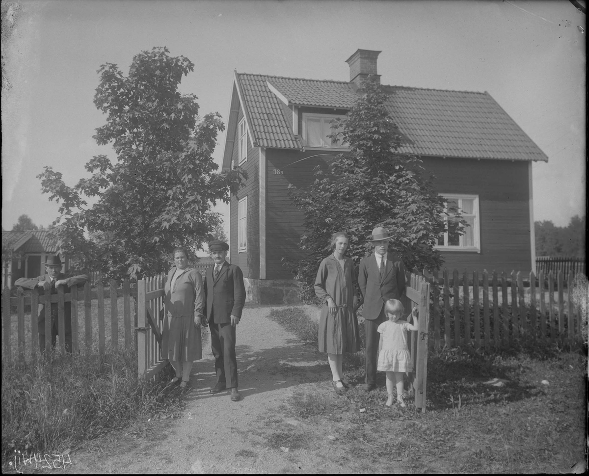Fotografering beställd av H. Olsson. Föreställer sannolikt Axel Hugo Olsson (1887-1959) och hans hustru Judit Katarina Höglin (1896-1965) till vänster. De andra är ej identifierade. Huset är idag rivet.
