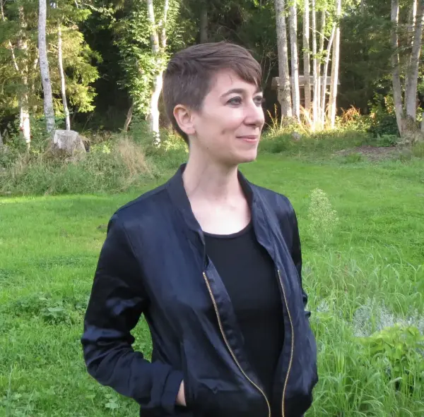 Ung kvinna som står på en gräsmatta med en skog i bakgrunden.