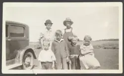 Familien Overland stående landbrukslandskap i Preeceville. Familie med fire barn. Bil stående på siden.