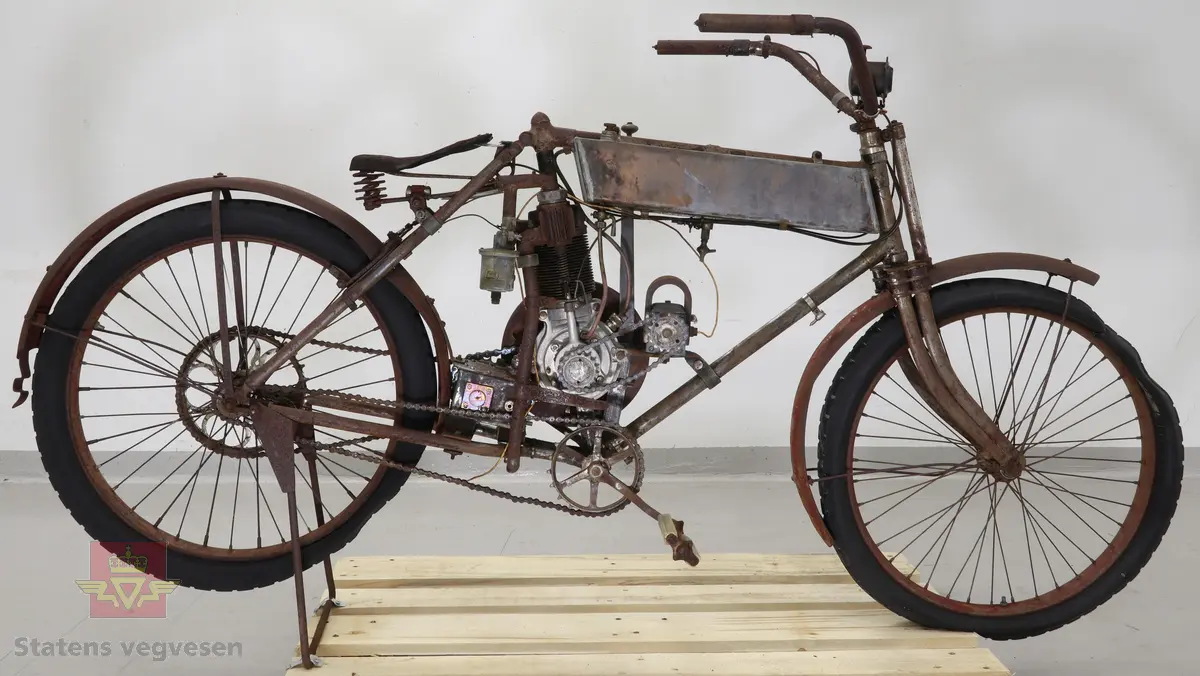 Motorsykkel med sort ramme og røde skjermer. Den har en enkel oppbygning som en motorisert tråsykkel med pedaler. Motor er en ensylindret firetaktsmotor, trolig en 120cc på 2  1/2 hk.
Motor er merket Lamaudiere no 528.
Opprinnelig var motorsykkelen levert med reimdrift, men har fått påbygd girkasse og kjededrift.
Bærer preg av lang tids lagring og har mye overflaterust. Motor og en del andre bevegelige deler sitter fastrustet.