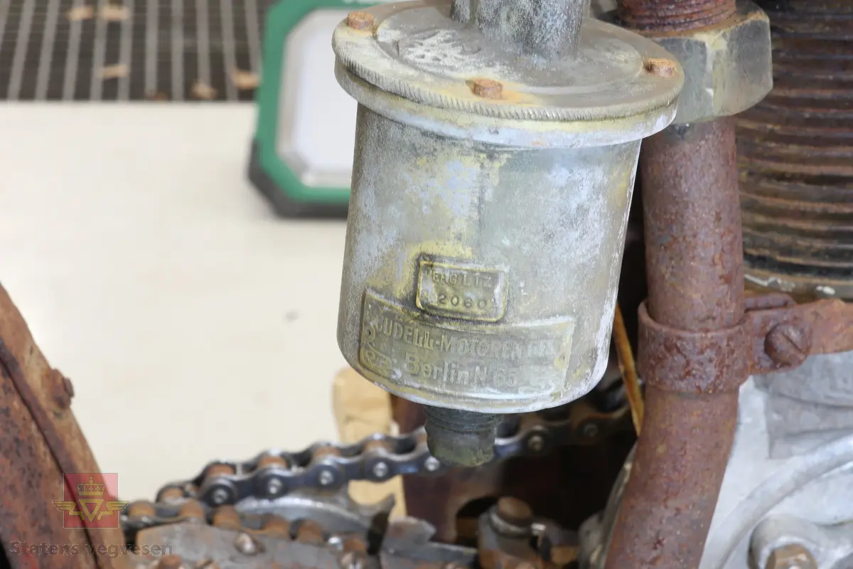 Motorsykkel med sort ramme og røde skjermer. Den har en enkel oppbygning som en motorisert tråsykkel med pedaler. Motor er en ensylindret firetaktsmotor, trolig en 120cc på 2  1/2 hk.
Motor er merket Lamaudiere no 528.
Opprinnelig var motorsykkelen levert med reimdrift, men har fått påbygd girkasse og kjededrift.
Bærer preg av lang tids lagring og har mye overflaterust. Motor og en del andre bevegelige deler sitter fastrustet.