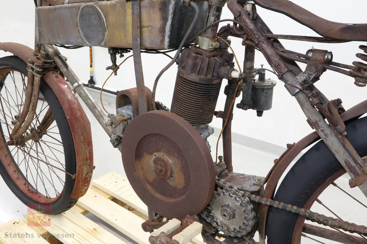 Motorsykkel med sort ramme og røde skjermer. Den har en enkel oppbygning som en motorisert tråsykkel med pedaler. Motor er en ensylindret firetaktsmotor, trolig en 120cc på 2  1/2 hk.
Motor er merket Lamaudiere no 528.
Opprinnelig var motorsykkelen levert med reimdrift, men har fått påbygd girkasse og kjededrift.
Bærer preg av lang tids lagring og har mye overflaterust. Motor og en del andre bevegelige deler sitter fastrustet.
