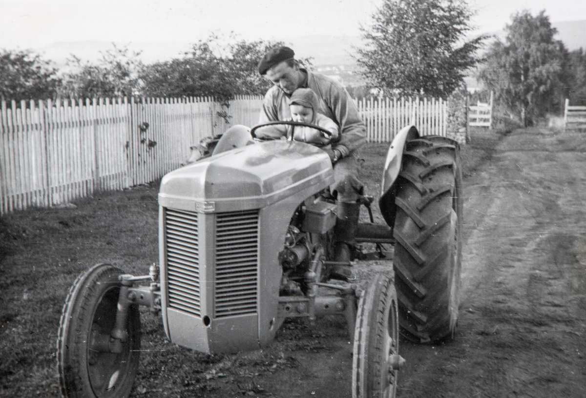 Ottar Landfald med sønnen Per-Otto Landfald på fanget kjører gårdens 1. traktor med gummihjul og bensinmotor, inne på tunet på Øvre Kaaterud gård.