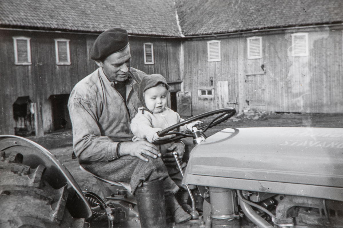 Ottar Landfald med sønnen Per-Otto Landfald på fanget kjører gårdens 1. traktor med gummihjul og bensinmotor, inne på tunet på Øvre Kaaterud gård.