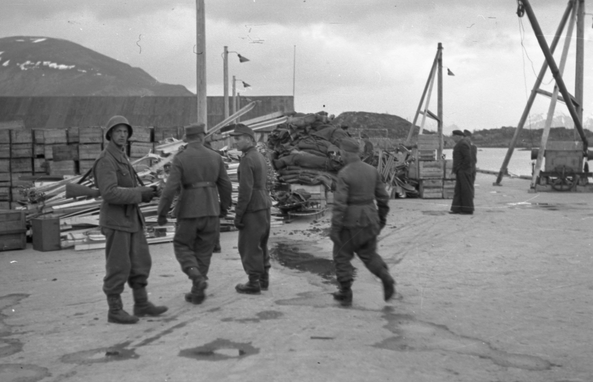 Norsk vaktsoldat på kaia sammen med tyske soldater. Større mengder med oppsamlet utstyr ligger i bakgrunnen. Dette utstyr ble etter hvert hentet av lasteskipet «Mungo» og sendt til Bodø.  
