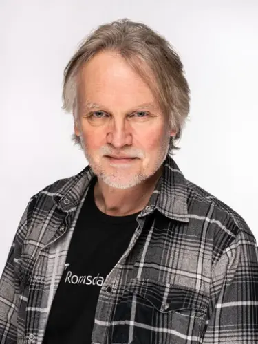 Portrett av an mann med grått hår og rutete skjorte.