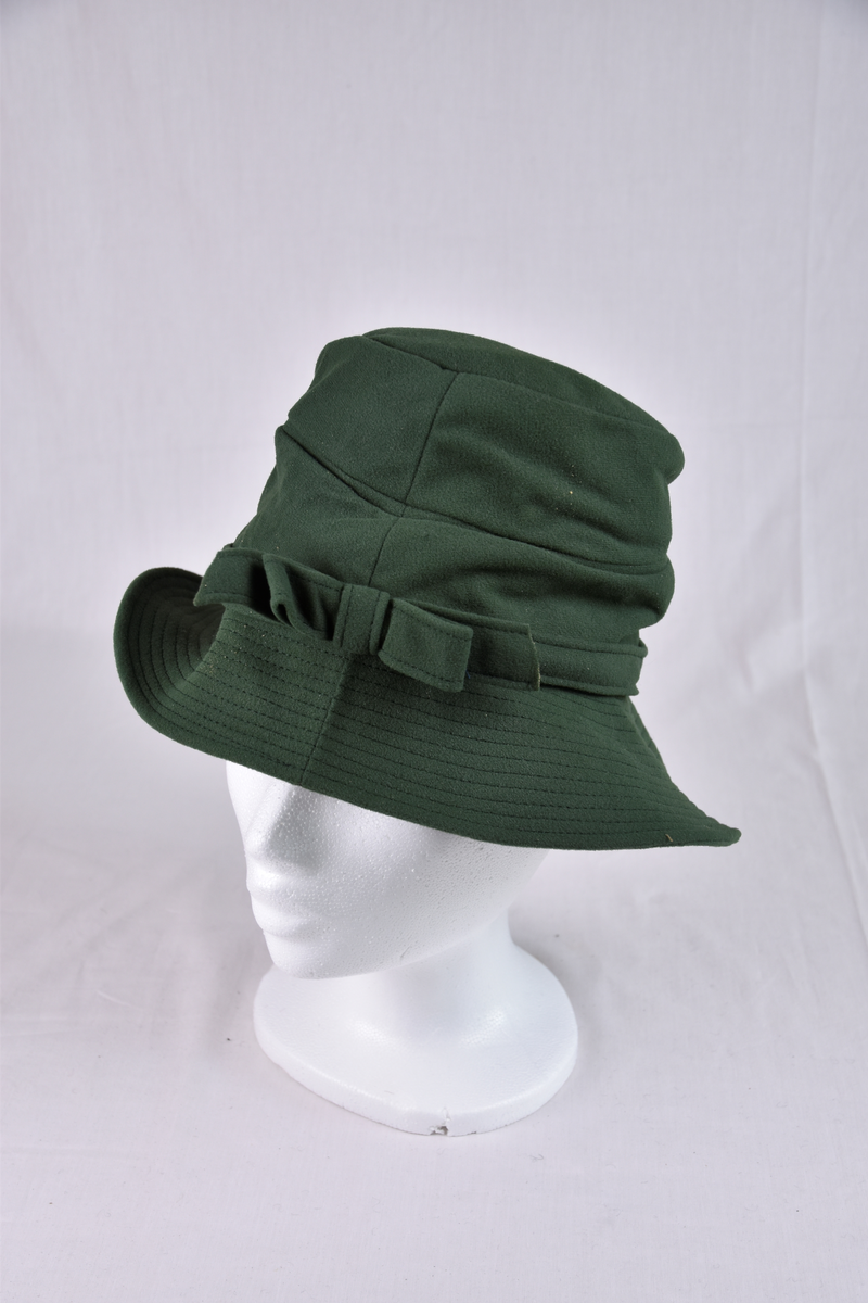 Hatt med flat topp og brem i grønn filt. Bånd med sløyfe rundt pullen.