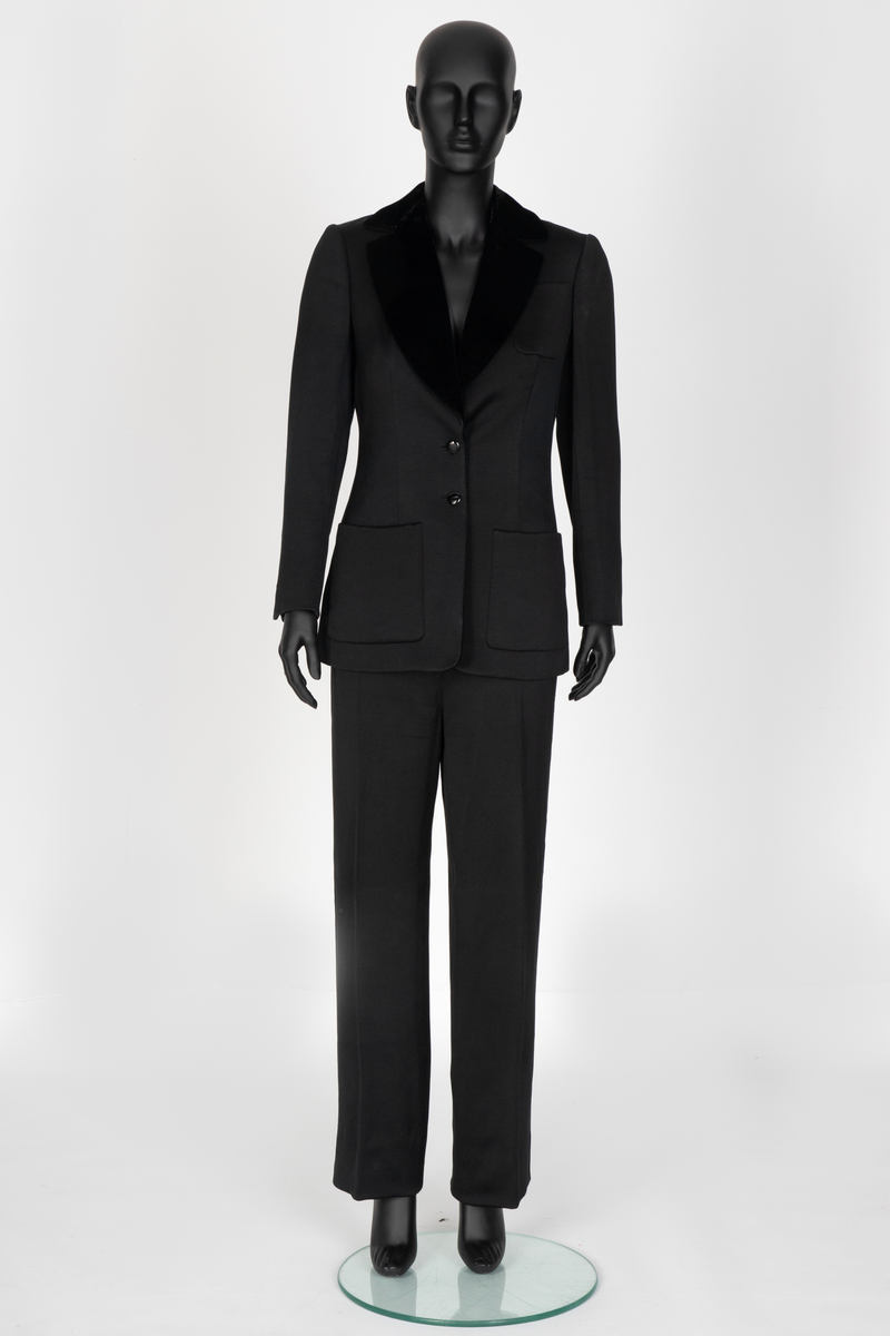 Smoking i svart silke- og ullsateng. Jakken har speilfløyelsslag og galloner. Enkeltspent med to knapper og tre lommer. Buksen har rette ben. Den er sydd ut i livet og linningen skjøtet på midt bak. Har hatt legg eller innsnitt foran. Tynn stripe i fløyel på siden av hvert bein.