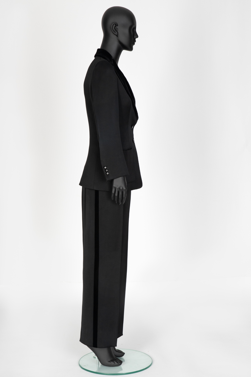 Smoking i svart silke- og ullsateng. Jakken har speilfløyelsslag og galloner. Enkeltspent med to knapper og tre lommer. Buksen har rette ben. Den er sydd ut i livet og linningen skjøtet på midt bak. Har hatt legg eller innsnitt foran. Tynn stripe i fløyel på siden av hvert bein.