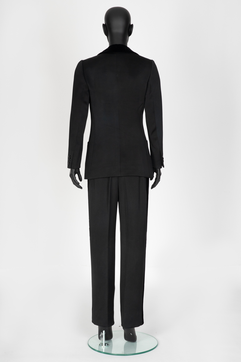 Smoking i svart silke- og ullsateng. Jakken har speilfløyelsslag og galloner. Enkeltspent med to knapper og tre lommer. Buksen har rette ben. Den er sydd ut i livet og linningen skjøtet på midt bak. Har hatt legg eller innsnitt foran. Tynn stripe i fløyel på siden av hvert bein.