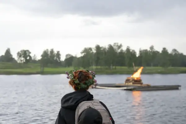 Person med blomsterkrans ser utover Bogstadvannet der Sankthansbålet brenner på en flåte.