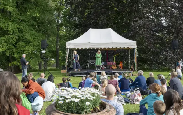 Publikum sitter på plenen og ser på sceneforestilling med Molly og Partner under Sankthansfeiring på Bogstad Gård.