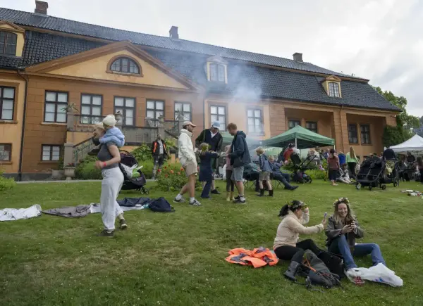 Besøkende samles foran hovedbygningen på Bogstad Gård med grilling, barnevogner og familieaktiviteter under Sankthansfeiring.