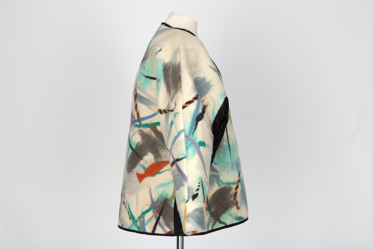 Jakke av filtet (tovet) ull. Ullstoffet har innlagte tråder i mange farger. Kimonofasong med innfelte stykker av blondestoff i sidene og under ermene. Halsen har asymmetrisk lukning mot venstre og jakken knappes foran med tre store plastknapper i passepoilerte knapphull. Forkanten på jakken har svarte kanter av blondestoffet. Jakken har rutete bomullsfôr.