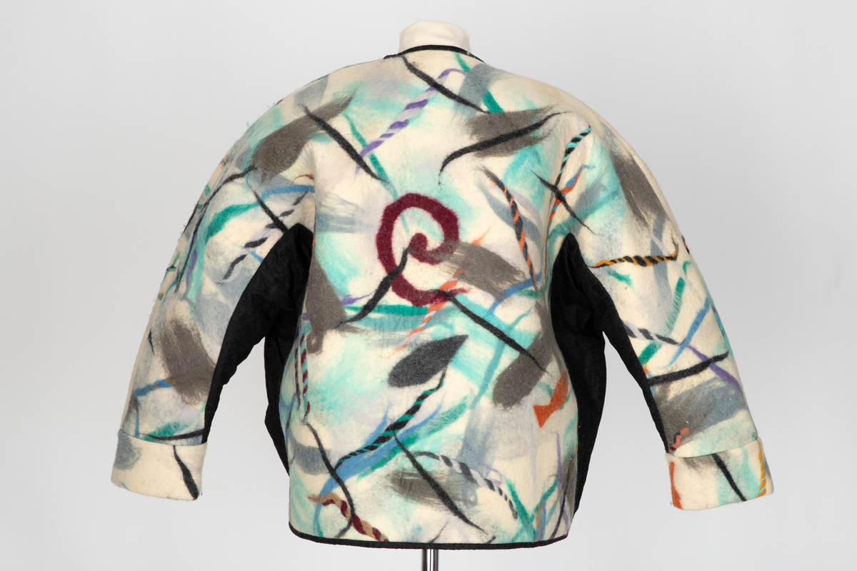 Jakke av filtet (tovet) ull. Ullstoffet har innlagte tråder i mange farger. Kimonofasong med innfelte stykker av blondestoff i sidene og under ermene. Halsen har asymmetrisk lukning mot venstre og jakken knappes foran med tre store plastknapper i passepoilerte knapphull. Forkanten på jakken har svarte kanter av blondestoffet. Jakken har rutete bomullsfôr.