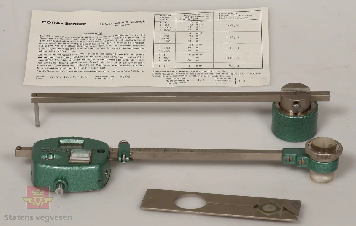 Planimeter av metall. Består av tre deler og garantikort. Ligger i et grått etui foret med rødt stoff på innsiden og låser av rustfritt stål. Hoveddelen har to roterende skalaer innebygd, og er malt med grønn hammerslagslakk. Ser ut til å være i topp stand. 

De andre delene i etuiet er som følge: 
NVM 01451 - 001 Metallstang med grønnmalt lodd i enden. Del av planimeter.
NVM 01451 - 002 Blank metallplate. Del av planimeter. 
NVM 01451 - 003 Garantikort av papir. Inneholder også noen tabeller. Svart skrift på hvit bakgrunn. 