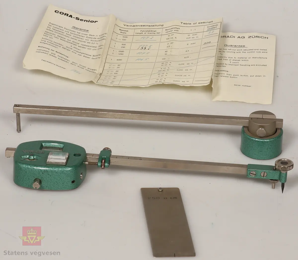 Planimeter av metall. Består av tre deler og garantikort. Ligger i et grått etui foret med rødt stoff på innsiden og låser av rustfritt stål. Hoveddelen har to roterende skalaer innebygd, og er malt med grønn hammerslagslakk. Ser ut til å være i topp stand. 

De andre delene i etuiet er som følge: 
NVM 01451 - 001 Metallstang med grønnmalt lodd i enden. Del av planimeter.
NVM 01451 - 002 Blank metallplate. Del av planimeter. 
NVM 01451 - 003 Garantikort av papir. Inneholder også noen tabeller. Svart skrift på hvit bakgrunn. 