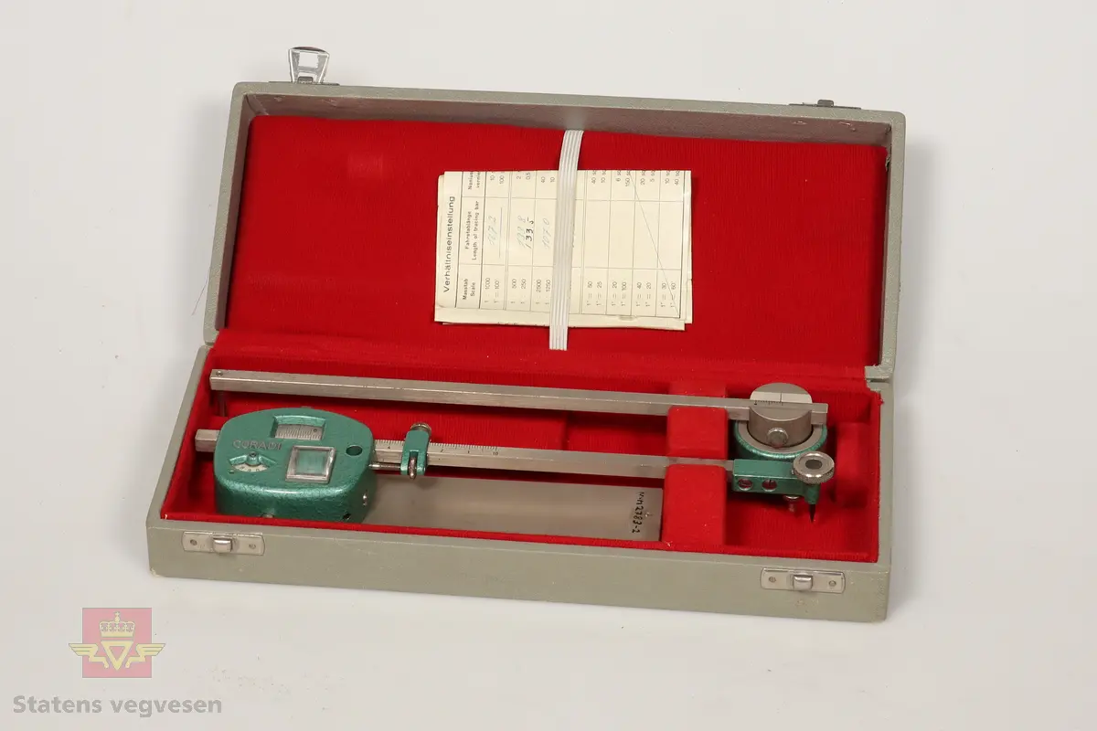 Planimeter av metall. Består av tre deler og garantikort. Ligger i et grått etui foret med rødt stoff på innsiden og låser av rustfritt stål. Hoveddelen har to roterende skalaer innebygd, og er malt med grønn hammerslagslakk. Ser ut til å være i topp stand. 

De andre delene i etuiet er som følge: 
NVM 01451 - 001 Metallstang med grønnmalt lodd i enden. Del av planimeter.
NVM 01451 - 002 Blank metallplate. Del av planimeter. 
NVM 01451 - 003 Garantikort av papir. Inneholder også noen tabeller. Svart skrift på hvit bakgrunn. 