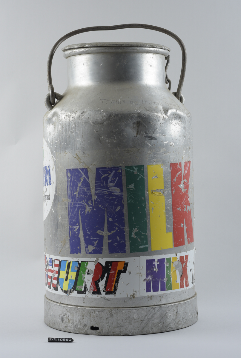 20 liters melkespann med hank og lokk. Flere klistremerker pålimt rundt hele.