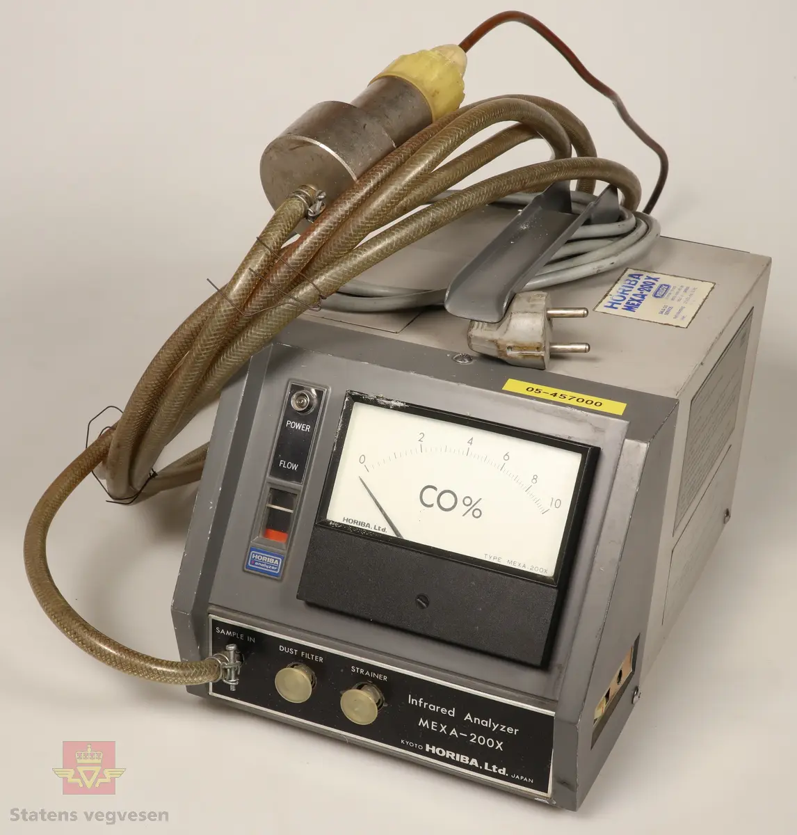 En avgassmåler for bensinmotorer av første generasjon. Innkapslet i plast, grå og svart. Har skala som viser Coprosenten. Grå 220 volt enfaskabel tilkoblet. Har 3,5 meter lang plastslange med vannfilter og føler tilkoblet. Føleren stikkes i eksosrøret. Målerne skal være helt i orden i følge giver. 