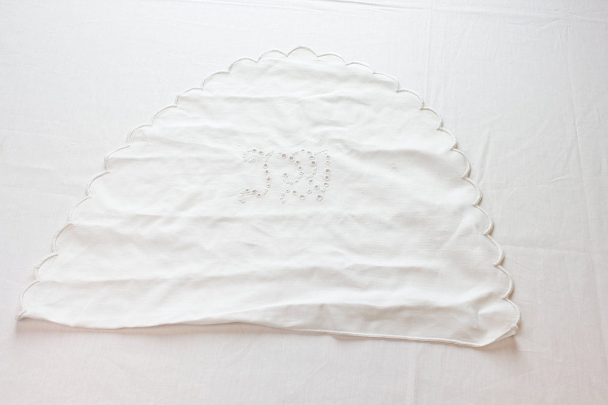 Hvit, halvsirkelformet brikke med brodert monogram.